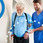 Caregiver assisting elderly man walking in a senior living facility hallway.