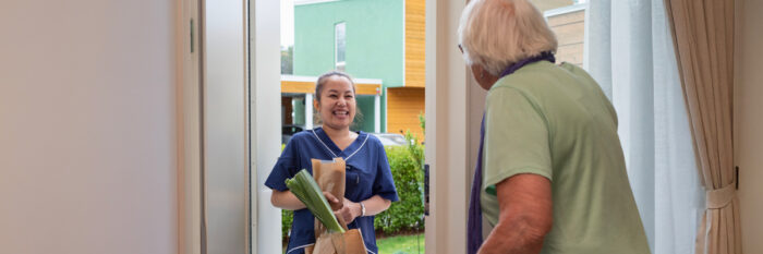 A caregiver is delivering groceries to a senior at their home.