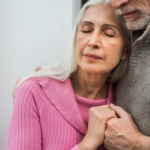 A senior couple is embracing one another.