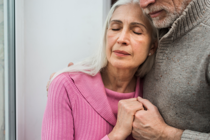 A senior couple is embracing one another.