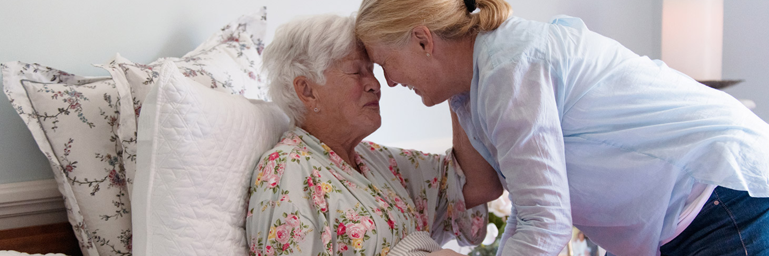 An adult child and their senior parent are embracing with their foreheads together.