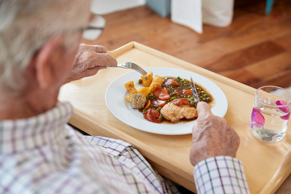 Over shoulder view of senior man eating dinner.