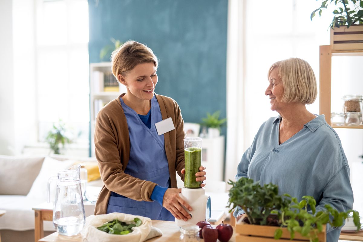 Senior woman with caregiver or healthcare worker making a smoothie.
